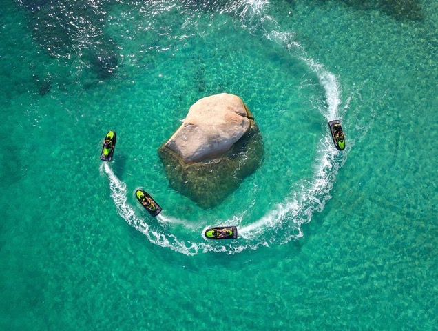  Vue aérienne de 4 jet-skis noir et vert contournant un rocher dans une eau de mer translucide