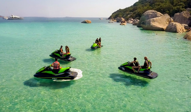  4 jet-skis noir et vert, sur lesquels sont réparties 7 personnes, arrêtés dans une crique et de l'eau turquoise à perte de vue